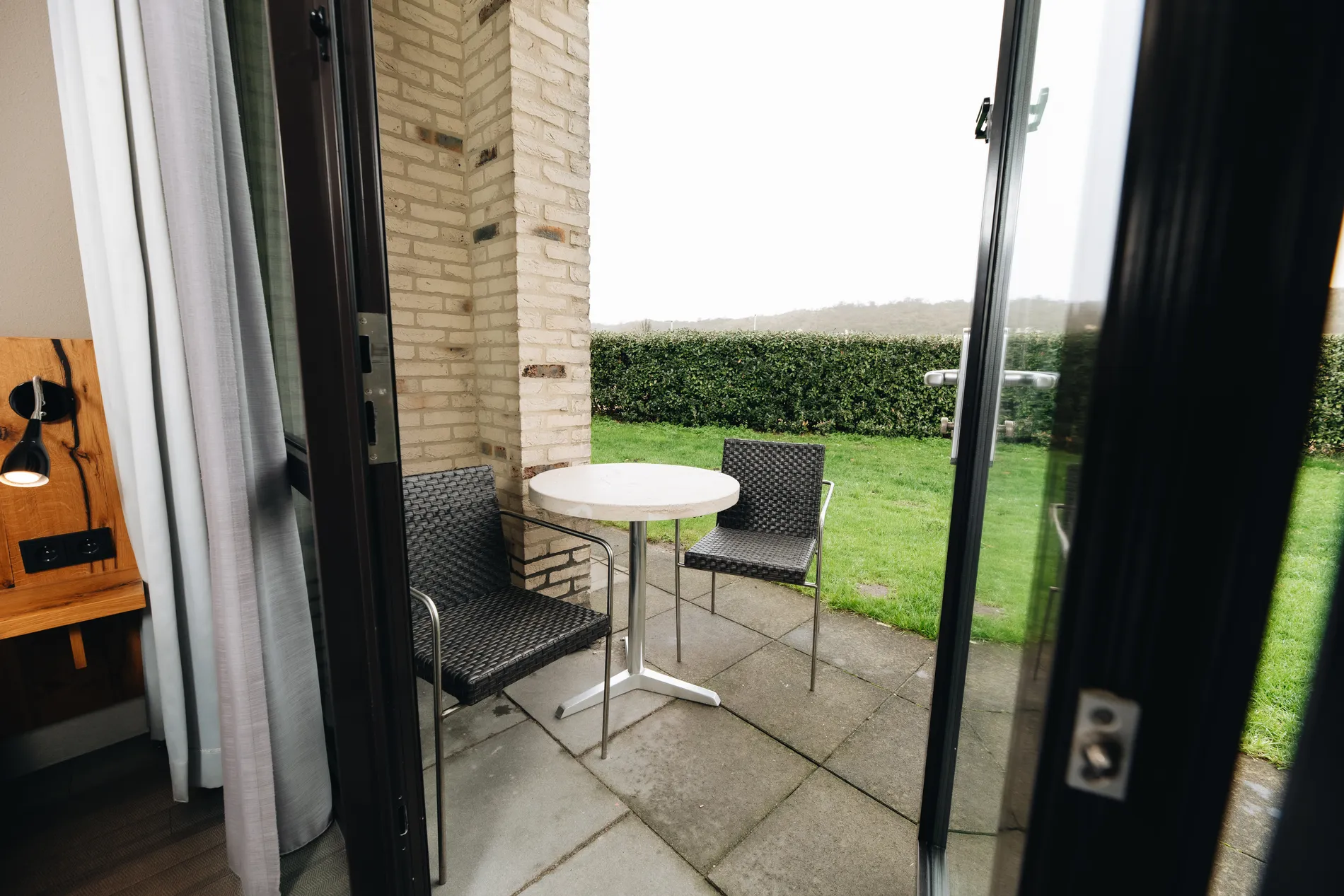 Privéterras bij een hotelkamer van Resort Land & Zee, voorzien van twee moderne kuipstoelen en een witte tafel, grenzend aan een gazon.